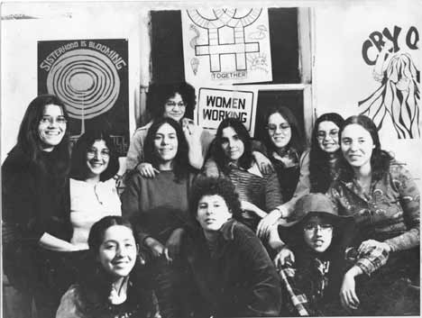 Members of the Chicago Women's Graphics Collective posing in front of signs they made in their print shop. The Collective