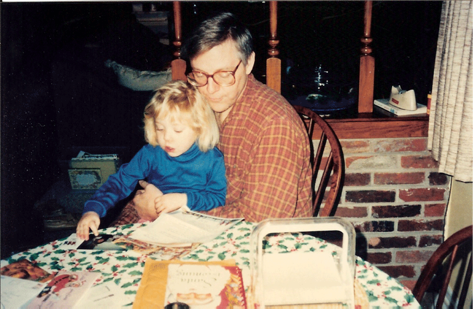 Rachel's dad sits at a table, her at a young age, maybe four or five, in his lap. she is touching a photo on the table, the outlines of her face and shirt are animated to blink in highlighted white