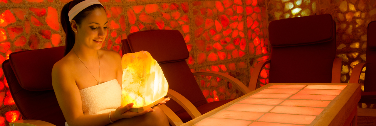 Extremely well-balanced and happy woman holding an enormous salt lamp, which is turned on and glowing all over her face and chest. She appears to be in a private room inside a spaceship.