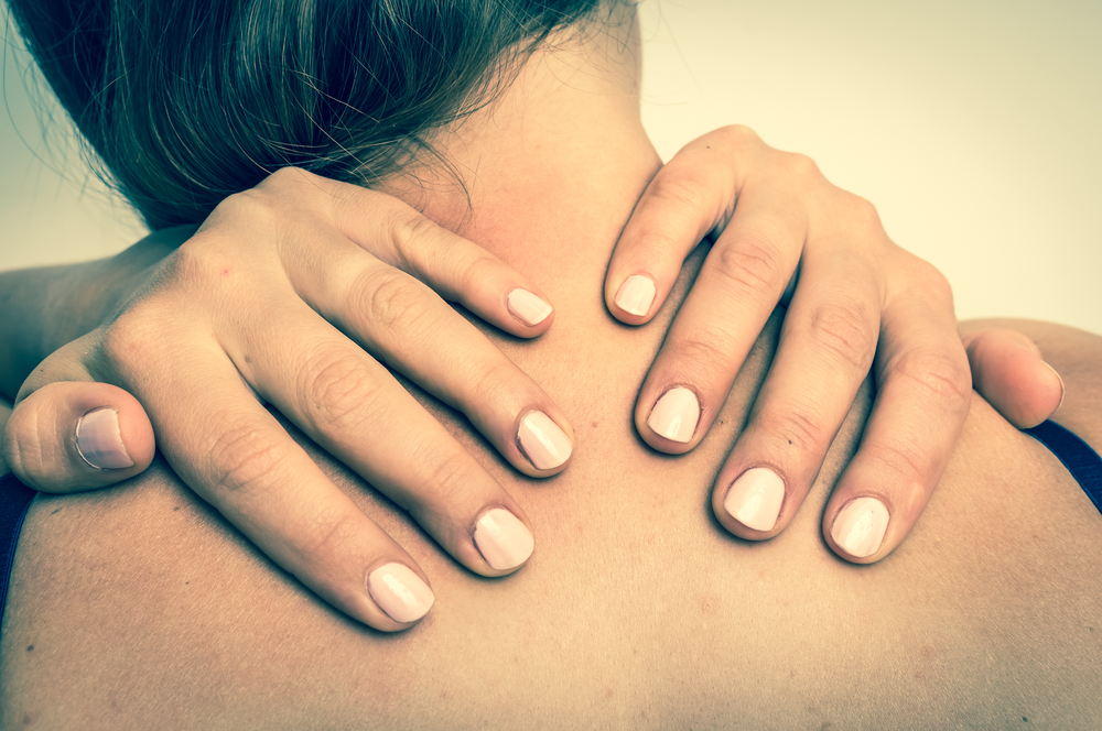 A woman with light skin and long, dark hair massages her neck with her hands.