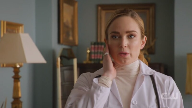 Sara presses the com in her ear and is dressed like a doctor