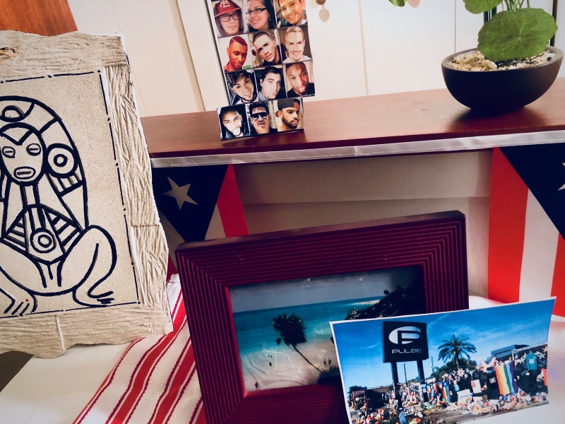 A home photograph of an altar built in a living room with a collection of white table cloth, candles, and Puerto Rican flags.