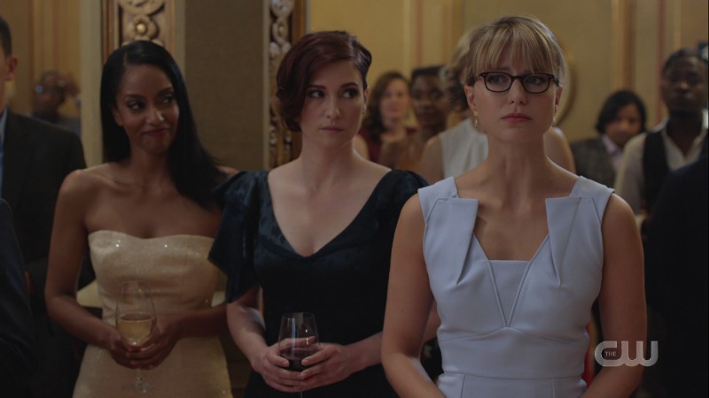 Kelly smiles while Alex looks worriedly at a half-broken Kara