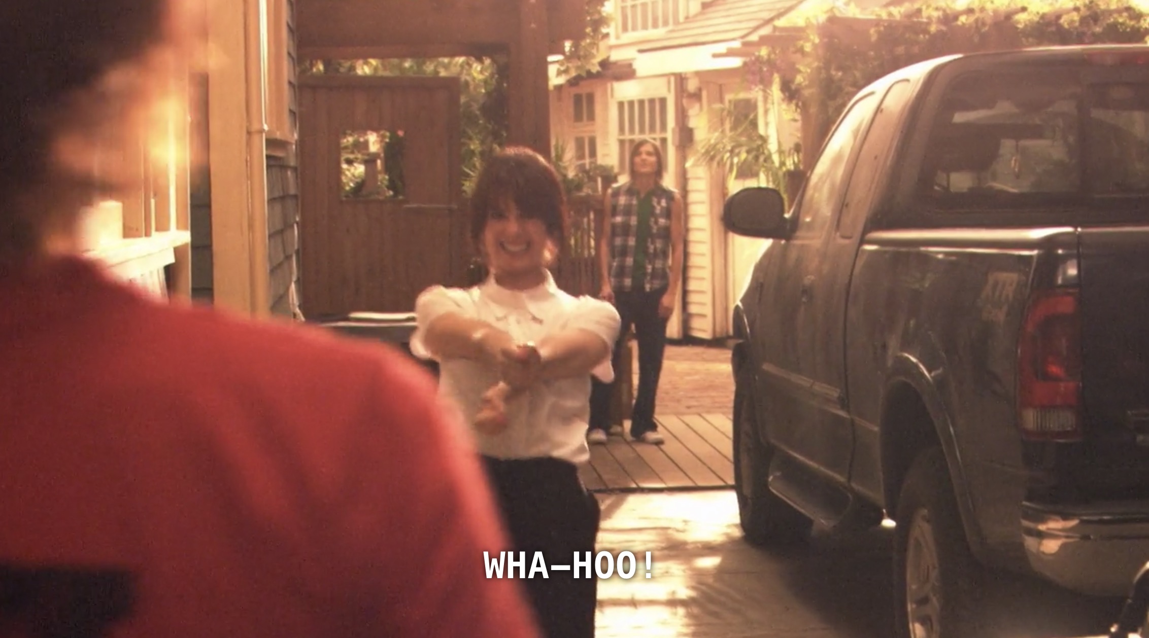 Jenny stands excitedly in the drive way next to a big pick-up truck, with Max standing behind her. Shane (wearing a red t-shirt with her back to the camera) has just arrived, and Jenny shouts excitedly, "Wha-hoo!"