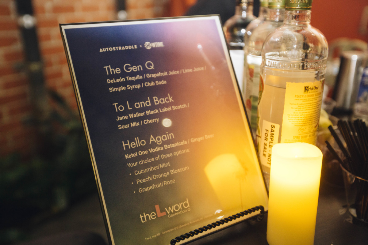 A photo of the drink menu with L Word-themed drinks, propped up next to a lit candle and bottles of liquor.