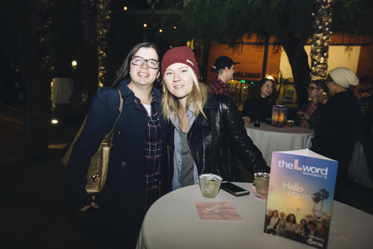 Two people pose for a photo, standing behind a tall circle cocktail table featuring drinks and a table topper advertising "The L Word: Generation Q"