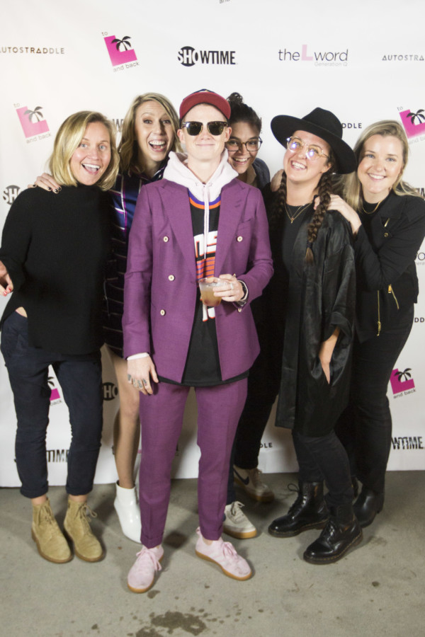 A group of 6 people all huddled together in front of a promo poster for "The L Word: Generation Q."