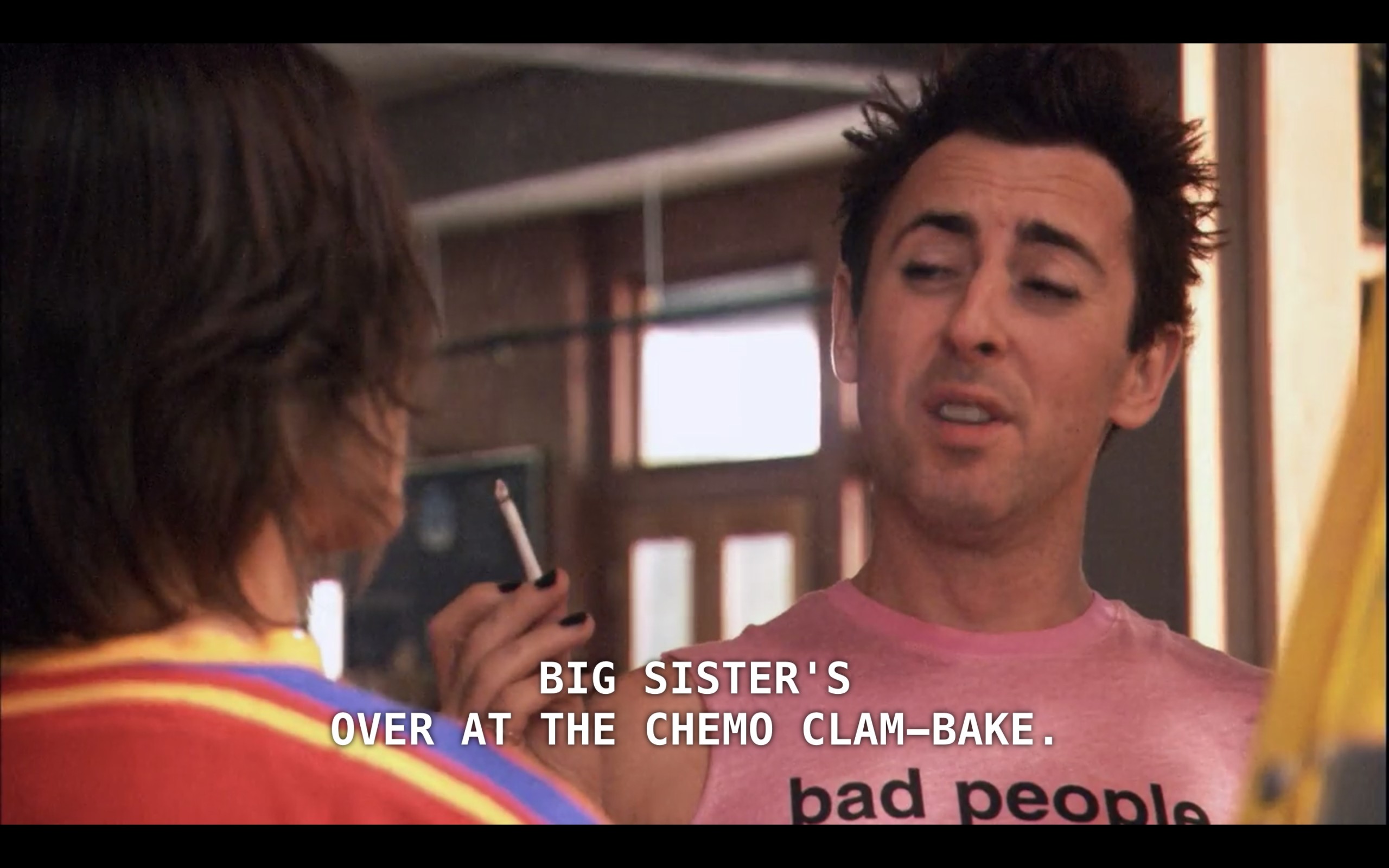 Billie is smoking a cigarette and wearing a pink tank top that says "bad people" on it. He is looking at Max, who is wearing a red shirt and whose back is to the camera. Billie says to him, "Big sister's over at the chemo clam-bake."