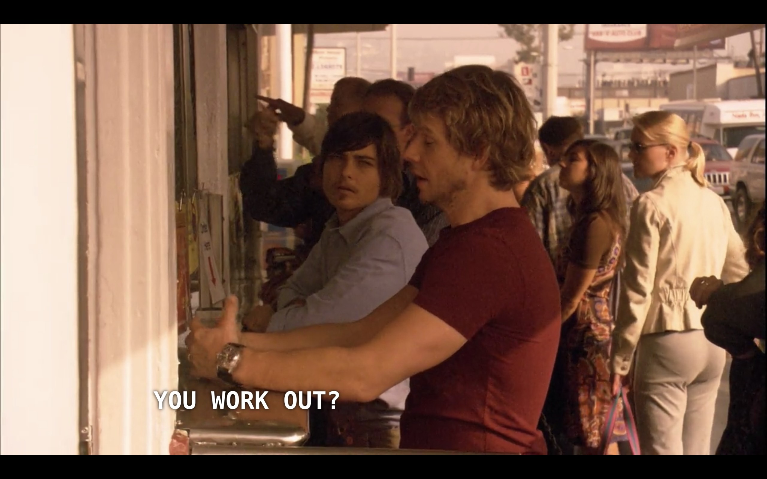 Tim (wearing a red t-shirt) and Max (wearing a blue button-up) stand at an outdoor bar. Max asks, "You work out?"