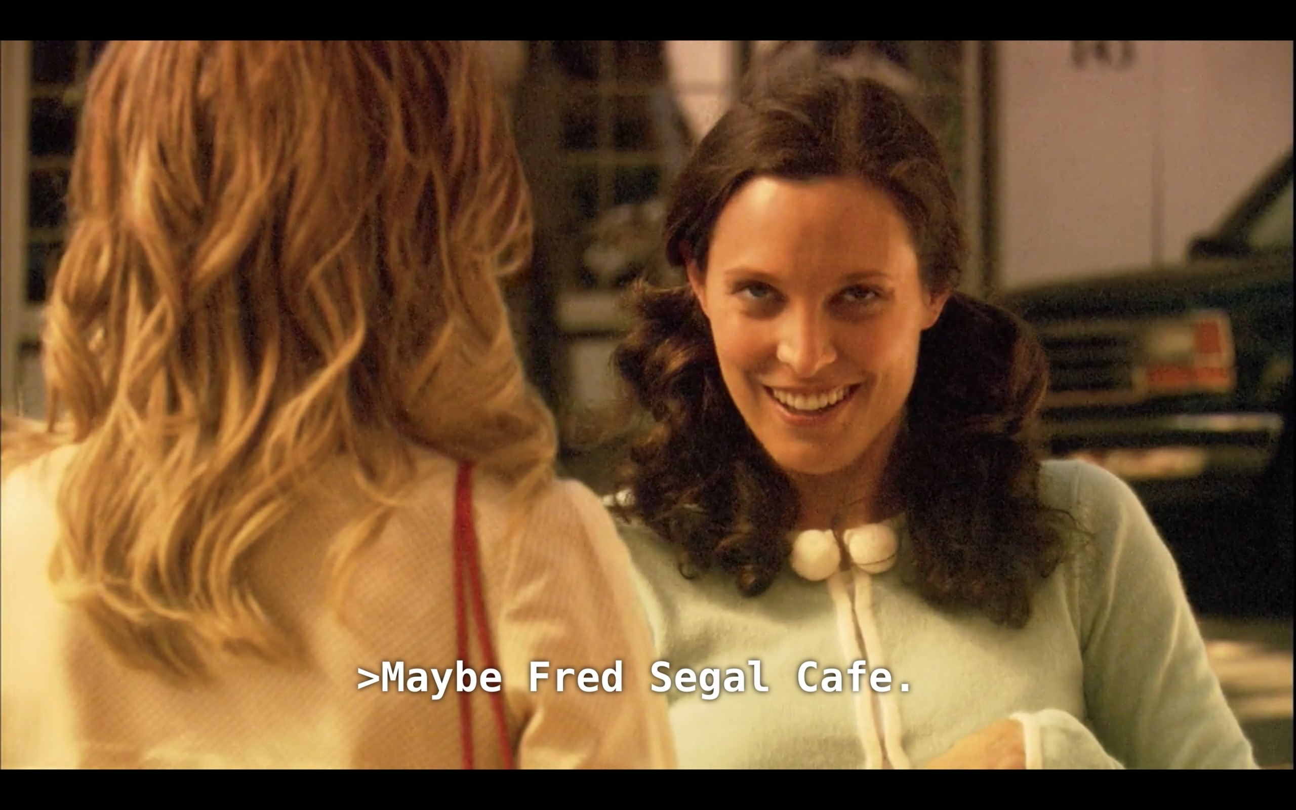 Dana (wearing pig tails and a light blue sweater) is looking at Alice (wearing a pink sweater, her back to the camera) with a sly look on her face. Dana says, "Maybe Fred Segal Cafe"