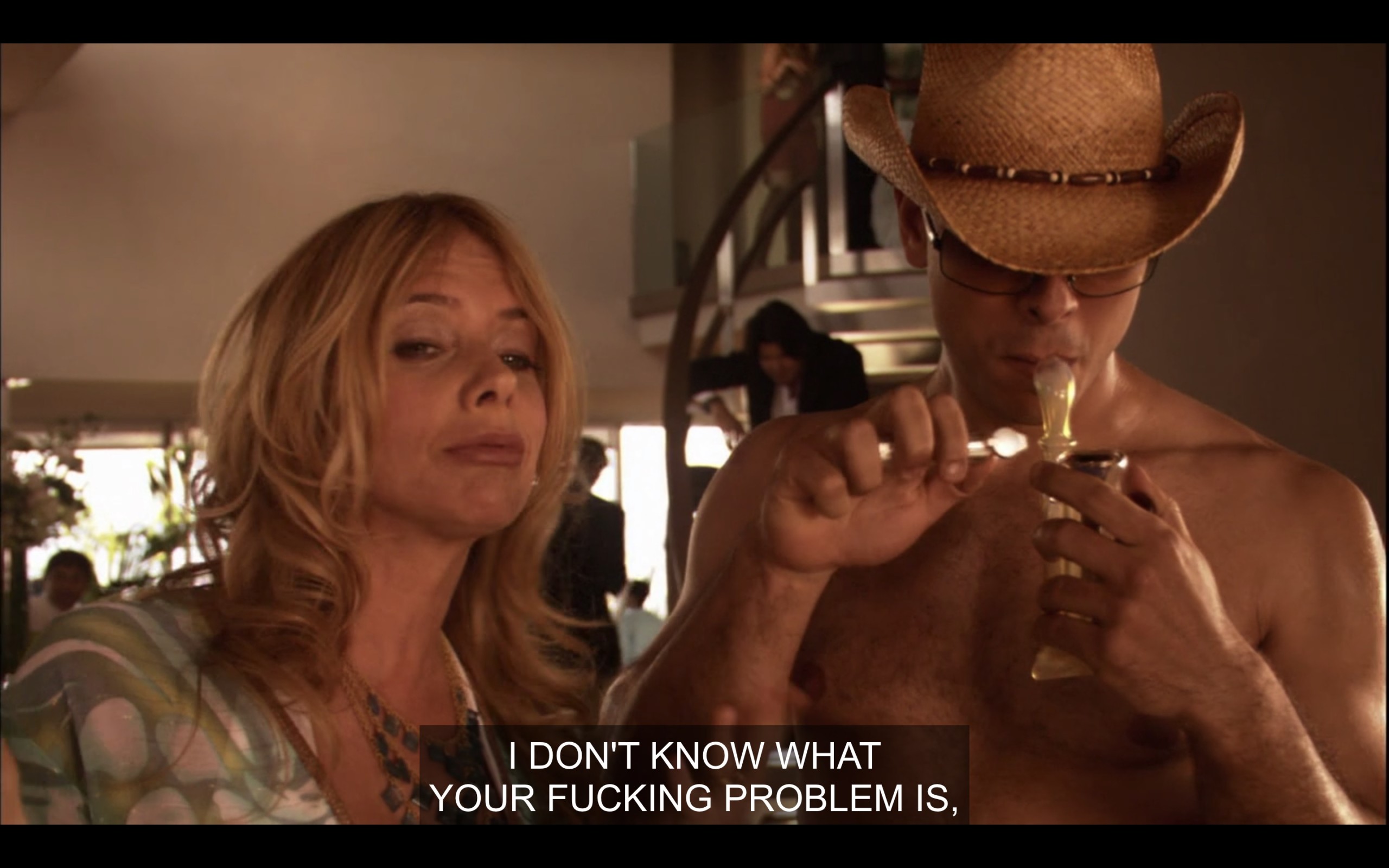 Cheri stands next to a topless guy wearing a cowboy hat and lighting a bong. Cheri says to Shane, who is off screen, "I don't know what your fucking problem is"