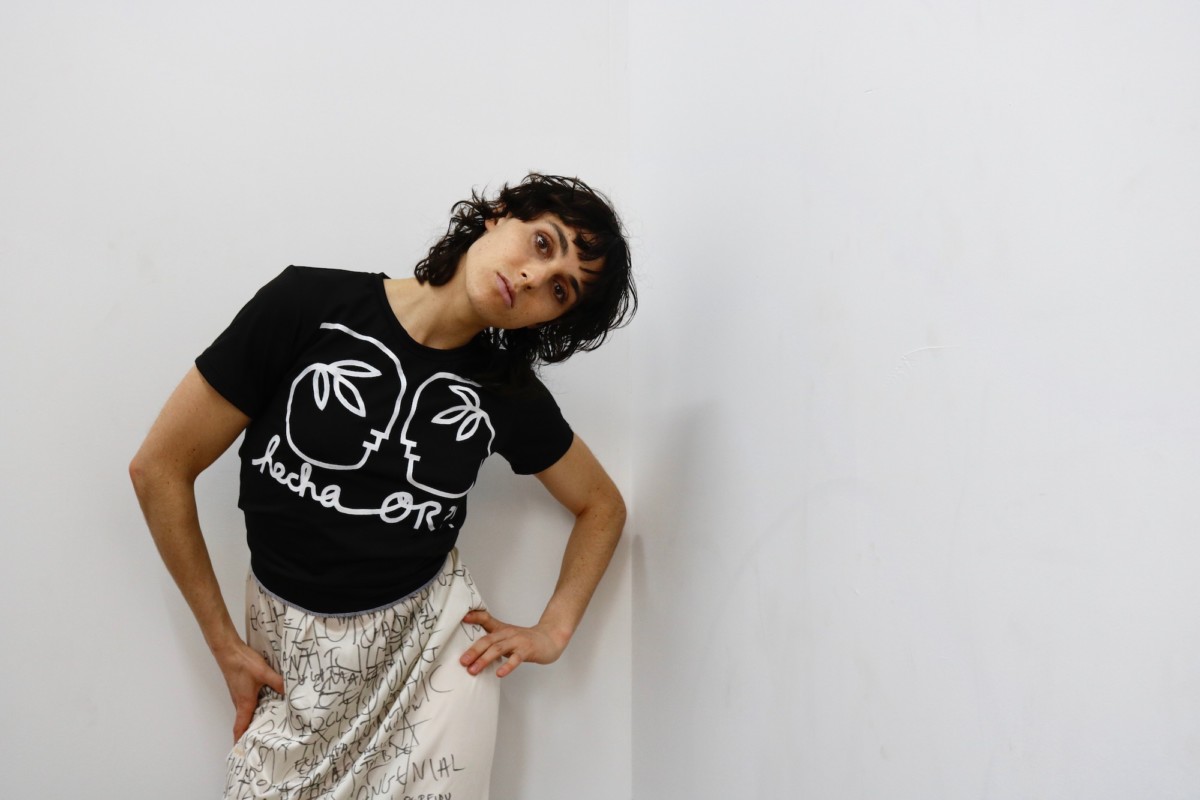 Model wears Official Rebrand black t shirt against a white wall.