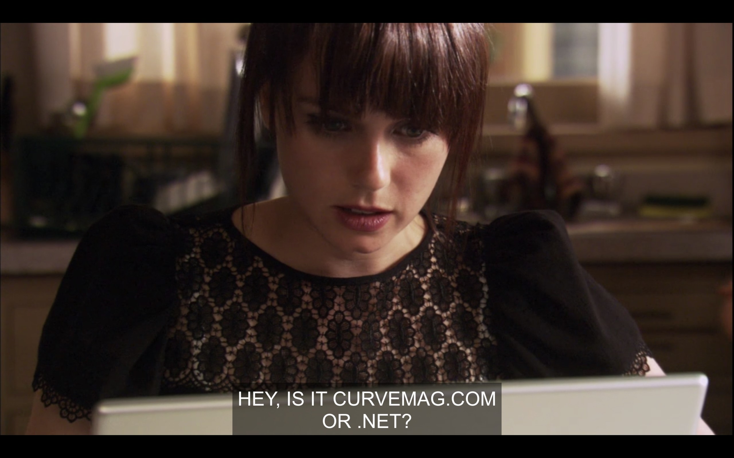 Jenny is wearing a black top and looking at her computer. She says, "Hey, is it CurveMag.com or .net?"