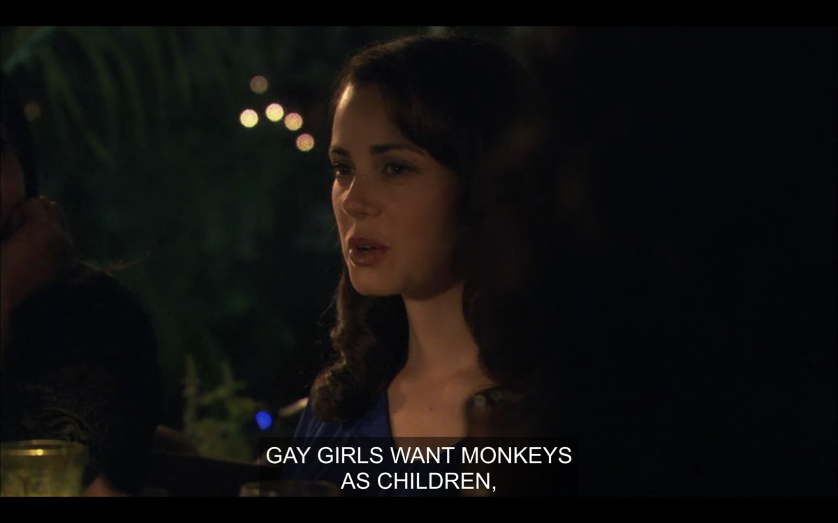 Catherine sitting at an outdoor dinner party table. She says, "Gay girls want monkeys as children."