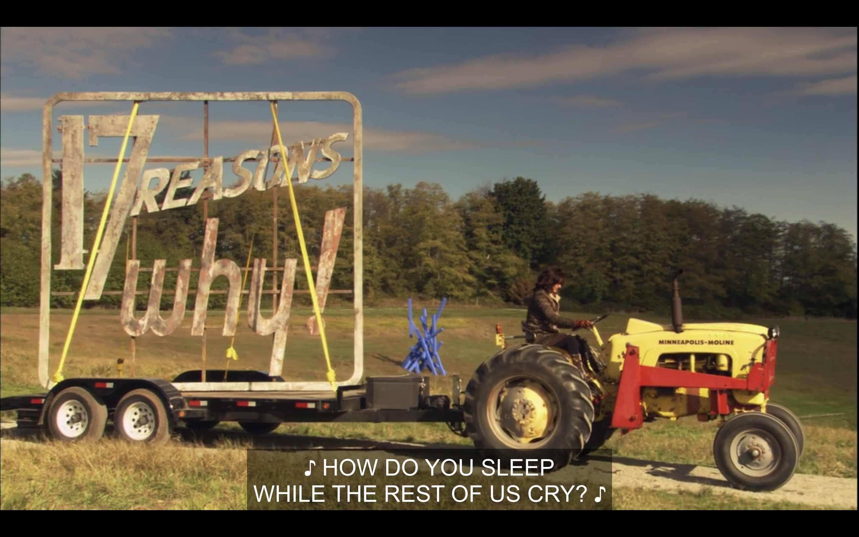 Bette is driving an enormous yellow tractor, with a trailer attached carrying the "17 reasons why!" billboard that they stole. Music plays in the background, singing, "How do you sleep while the rest of us cry?"