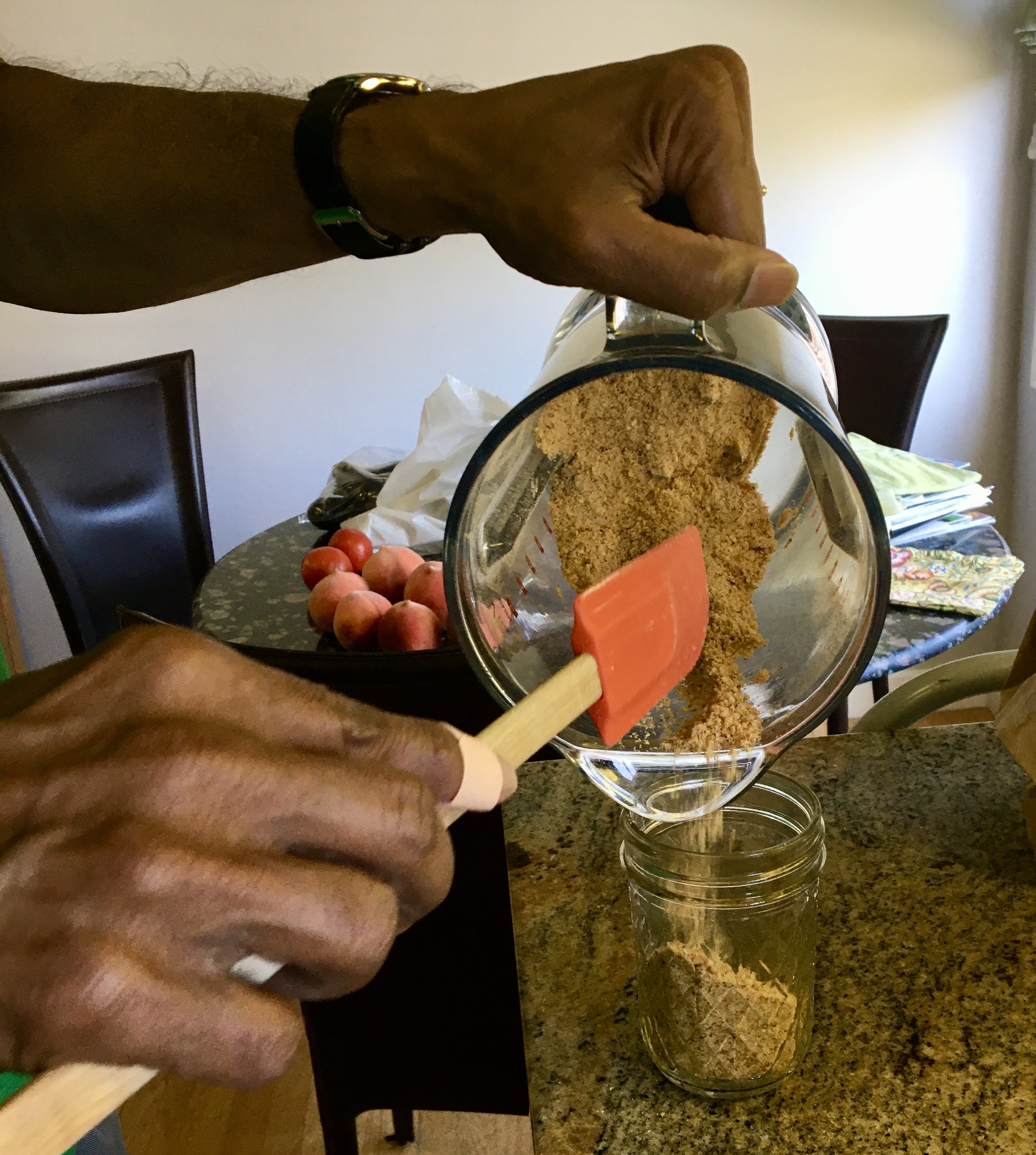one brown hands shovels gunpowder from a blender into a small ball jar with an orange spatula