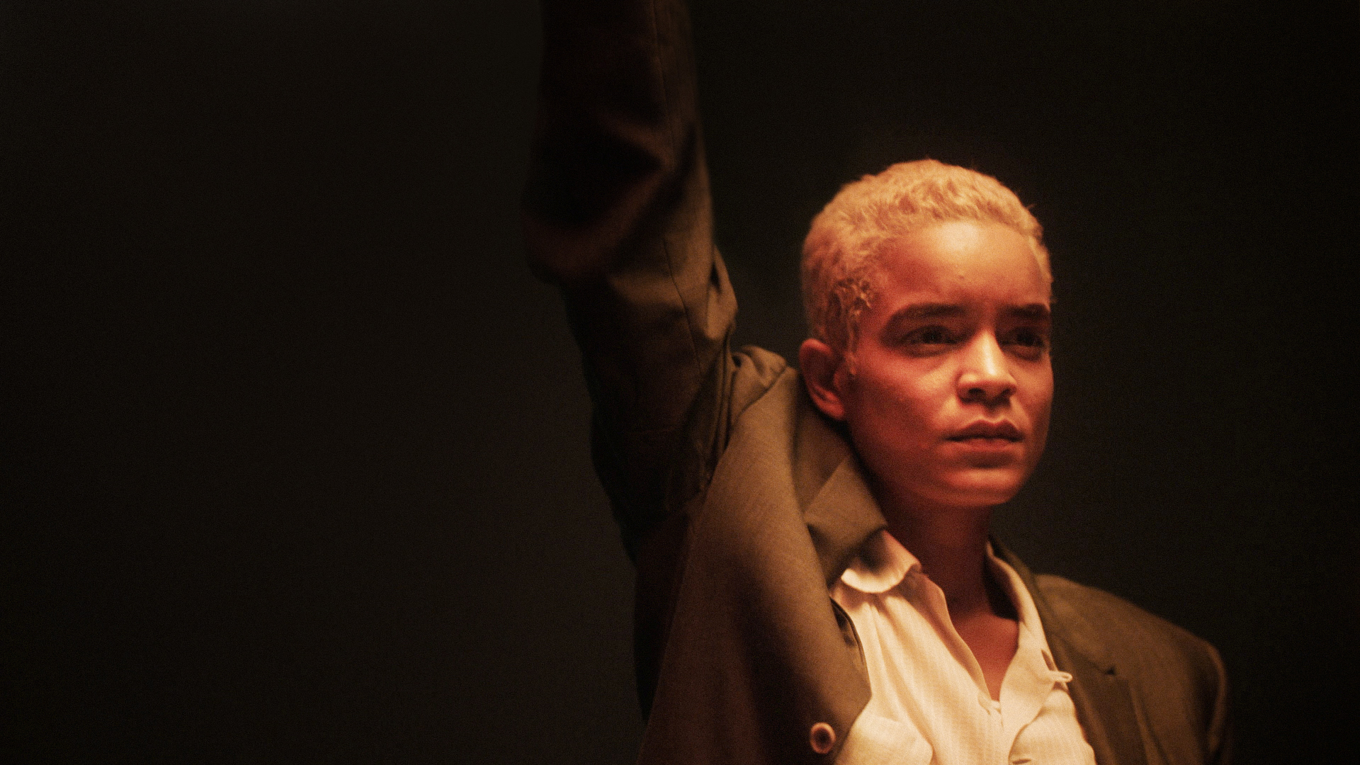 Elizabeth Faith Ludlow as Stormé DeLarverie, wearing a suit and shirt with her arm in the air