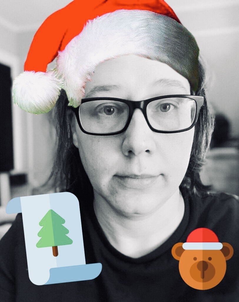 A Black and White photograph of Heather Hogan, with a bright red Santa hat photoshopped onto her head in the style of emoji animation.