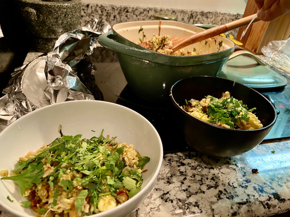 a bowl of yellow rice topped with herbs getting served from a dutch oven on the stove top