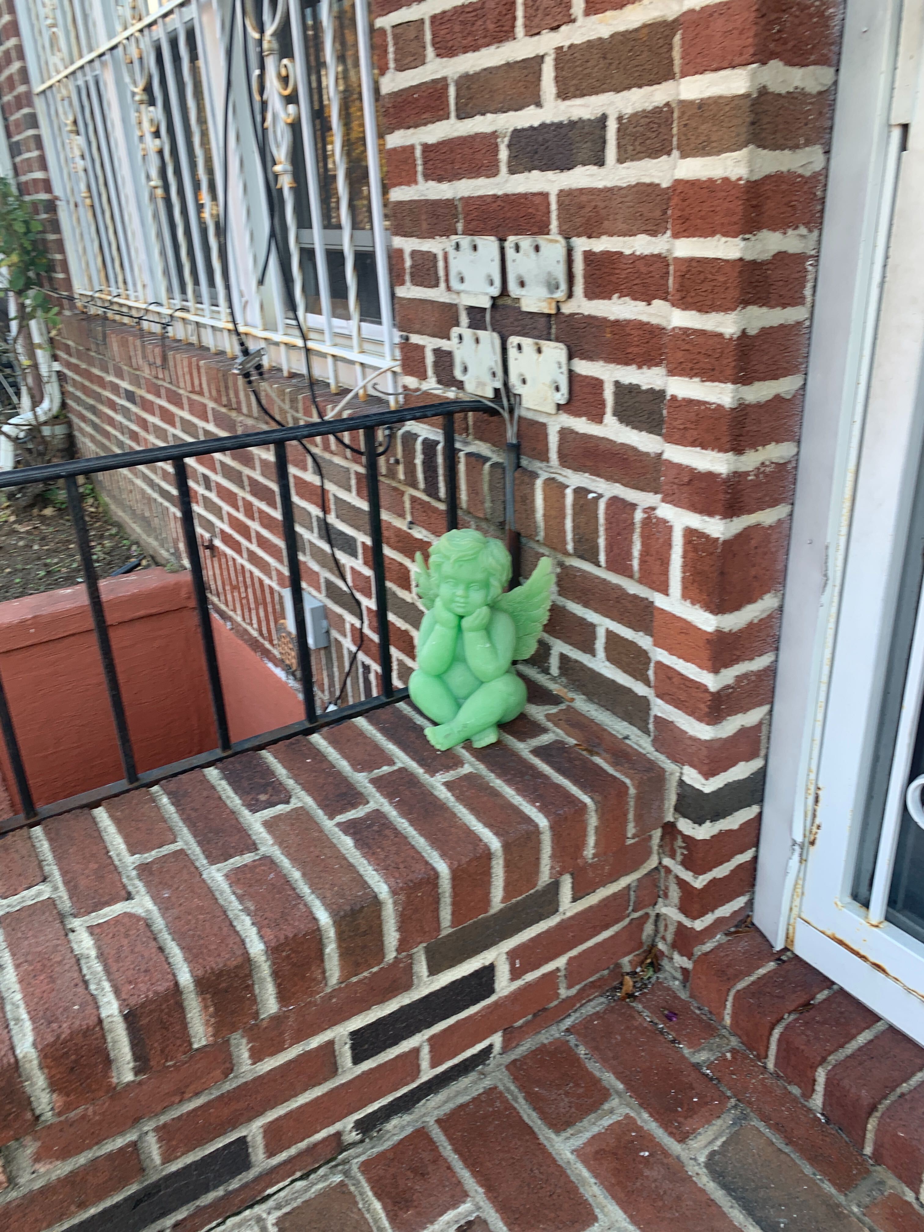 A pale lime green cherub sitting with its legs crossed on a brick stoop.