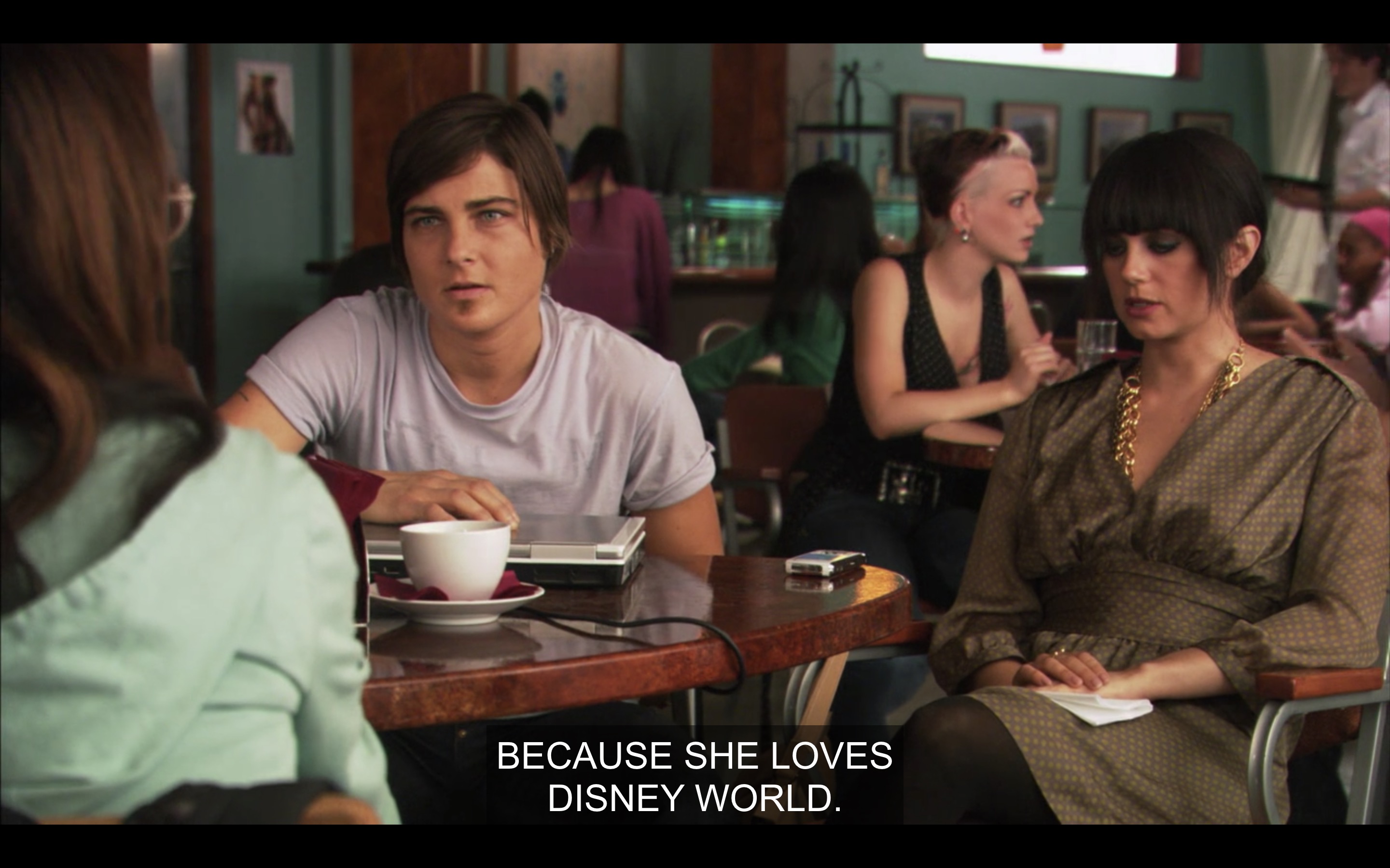 Max and Jenny are sitting at a table at The Planet with Adele, whose back is to the camera. "Because she loves Disney World."