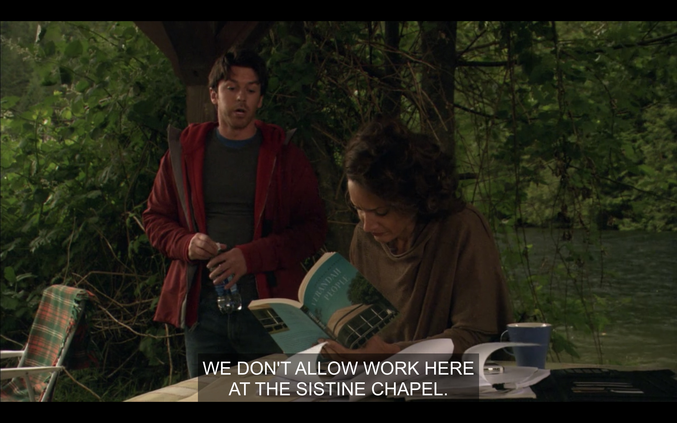 A man in a hoodie tells Bette, who is sitting at a picnic table reading a novel and taking notes, that they don't allow work here.
