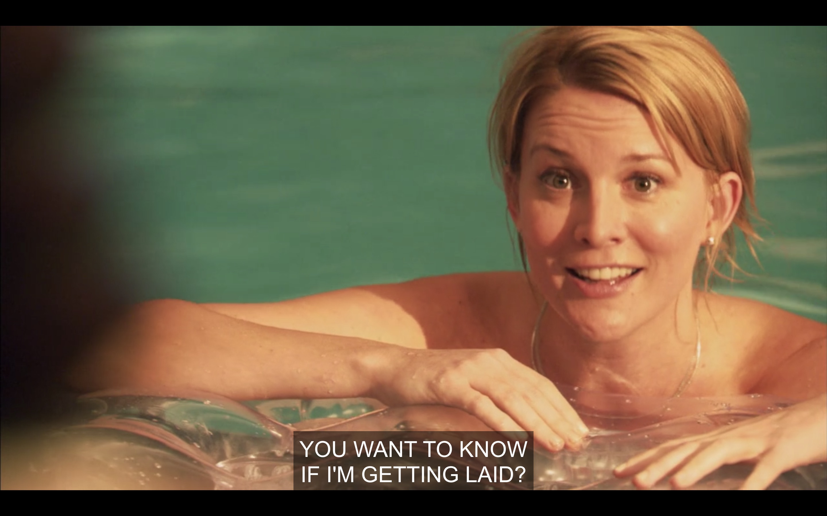 Tina topless in the pool with her arms resting on a float, saying "You want to know if I'm getting laid?"