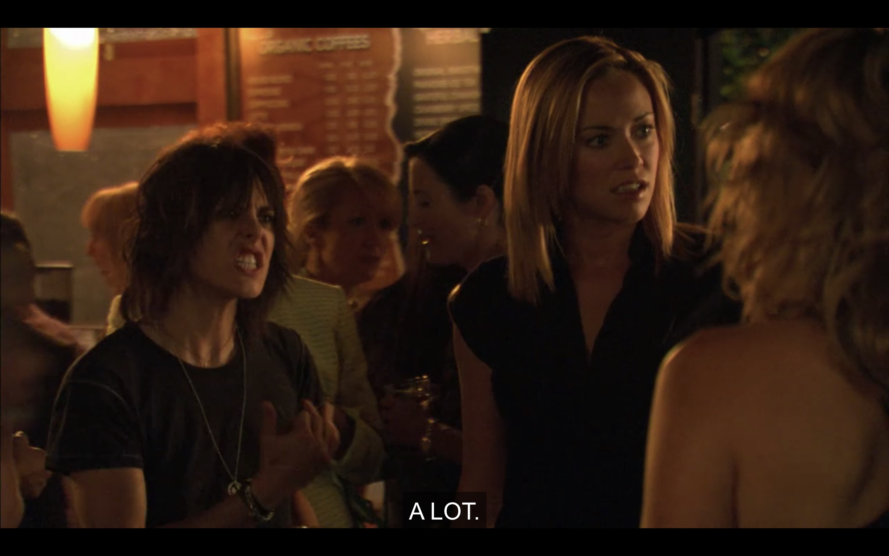 At a party. Shane's teeth are gritted, she's wearing a t-shirt, she's holding her hand out in some gesture while Paige, aghast, looks at her friends for support.