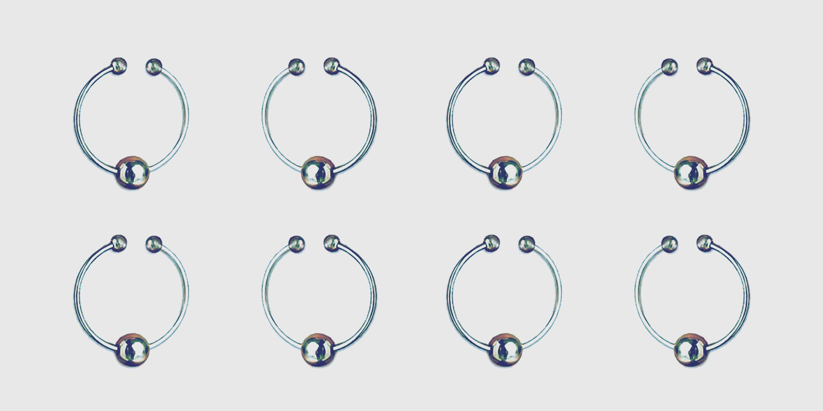An array of small stainless steel nipple rings with an opening in ring to be worn or removed, and a single steel ball dangling on the hooped ring