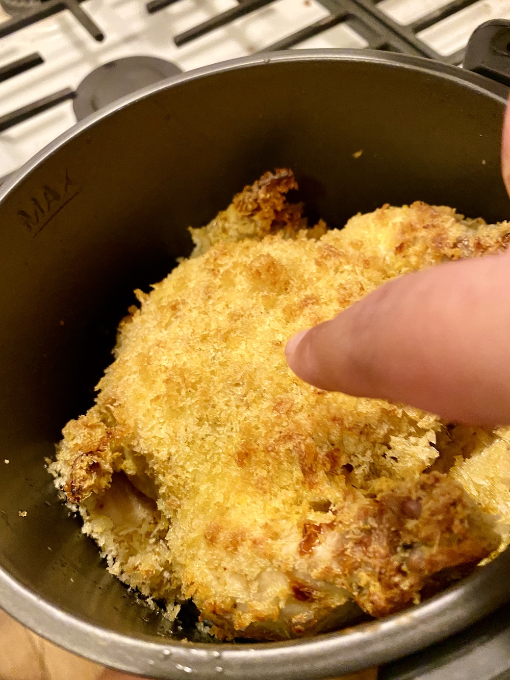 a finger pointing at the crispy, breaded outside of finished air-fried game hen