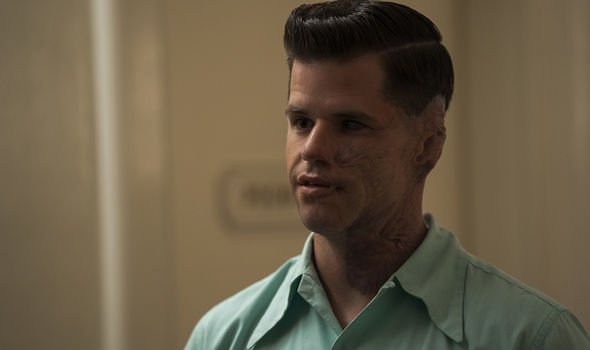 Charlie Carver as Huck in the Netflix show "Ratched." He stares off to the left in a light blue colored shirt and has brunette hair in a close cut style of the 1940s.