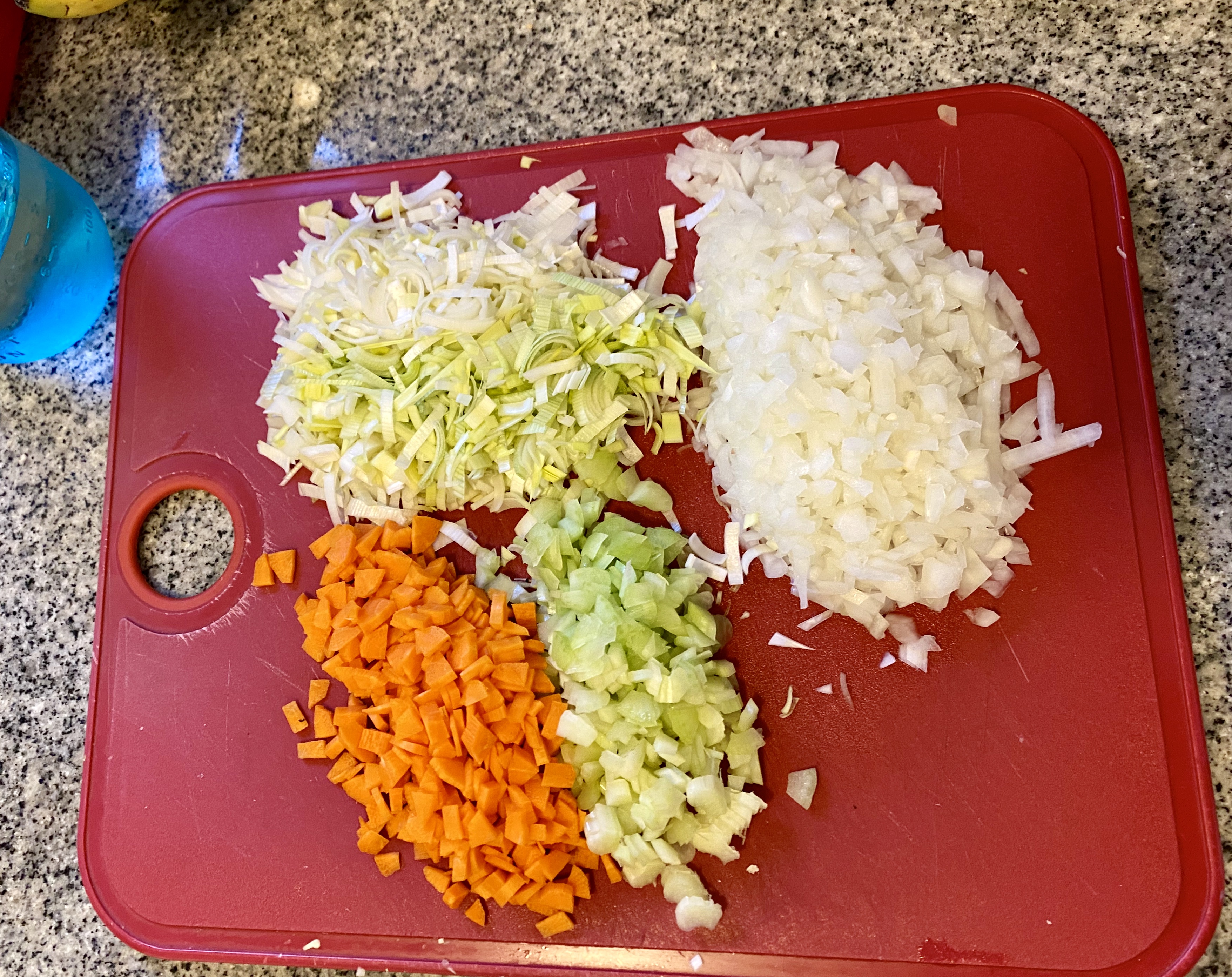 a read cutting board with piles of chopped carrots, leek, celery and onion