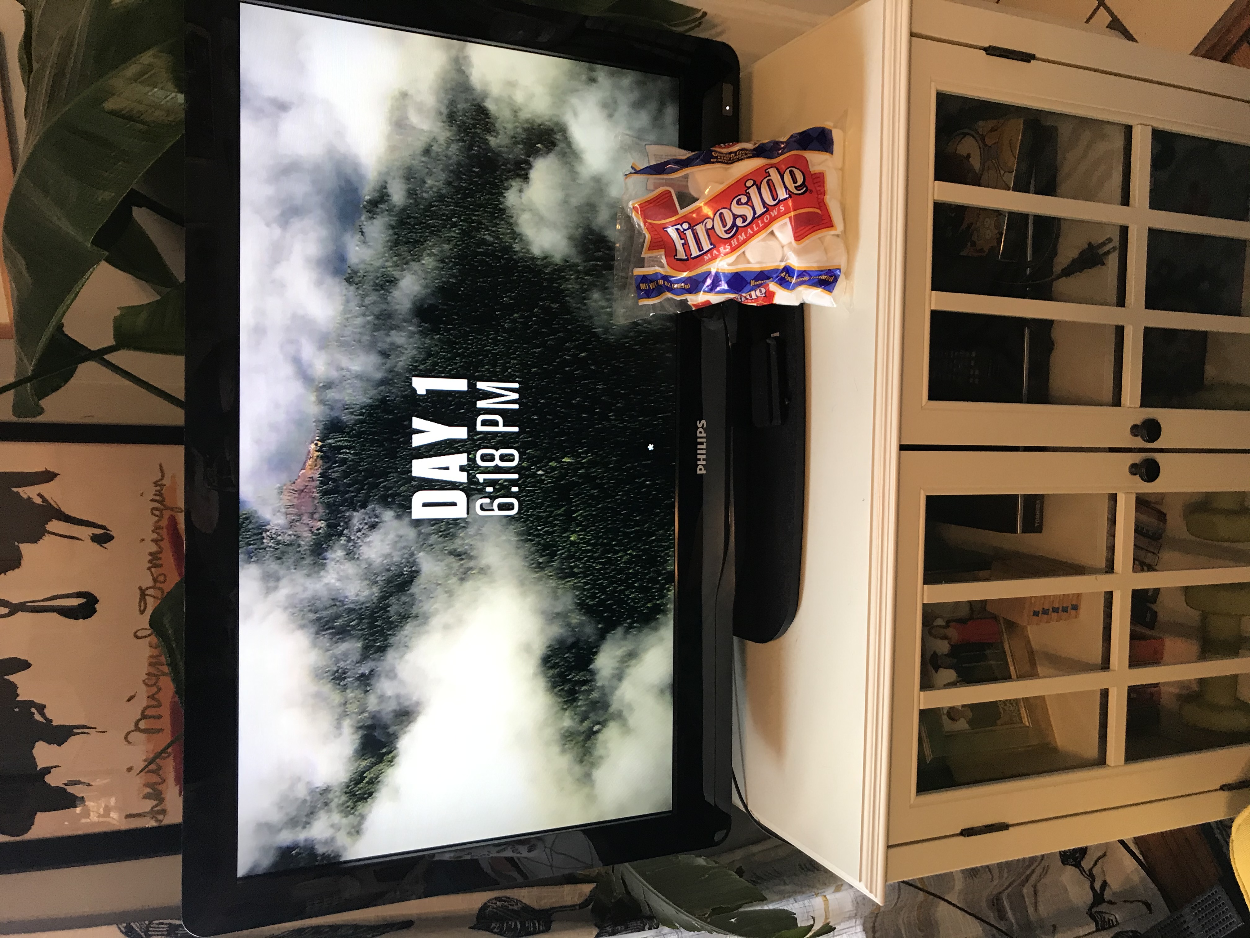 A bag of marshmallows propped up against a tv screen showing an outdoors reality show.