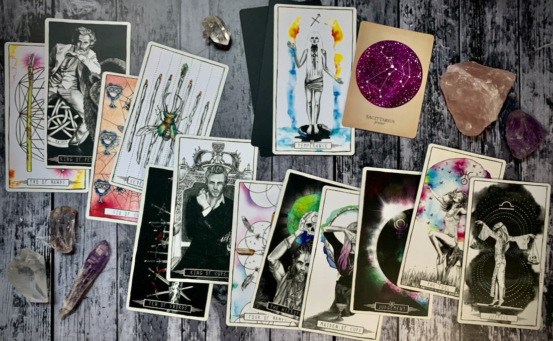 A photo of a scattered deck of Tarot cards and crystals across a distressed wood table