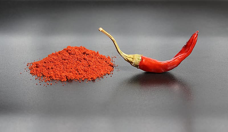 a mound of red chilli powder next to a whole red chilli