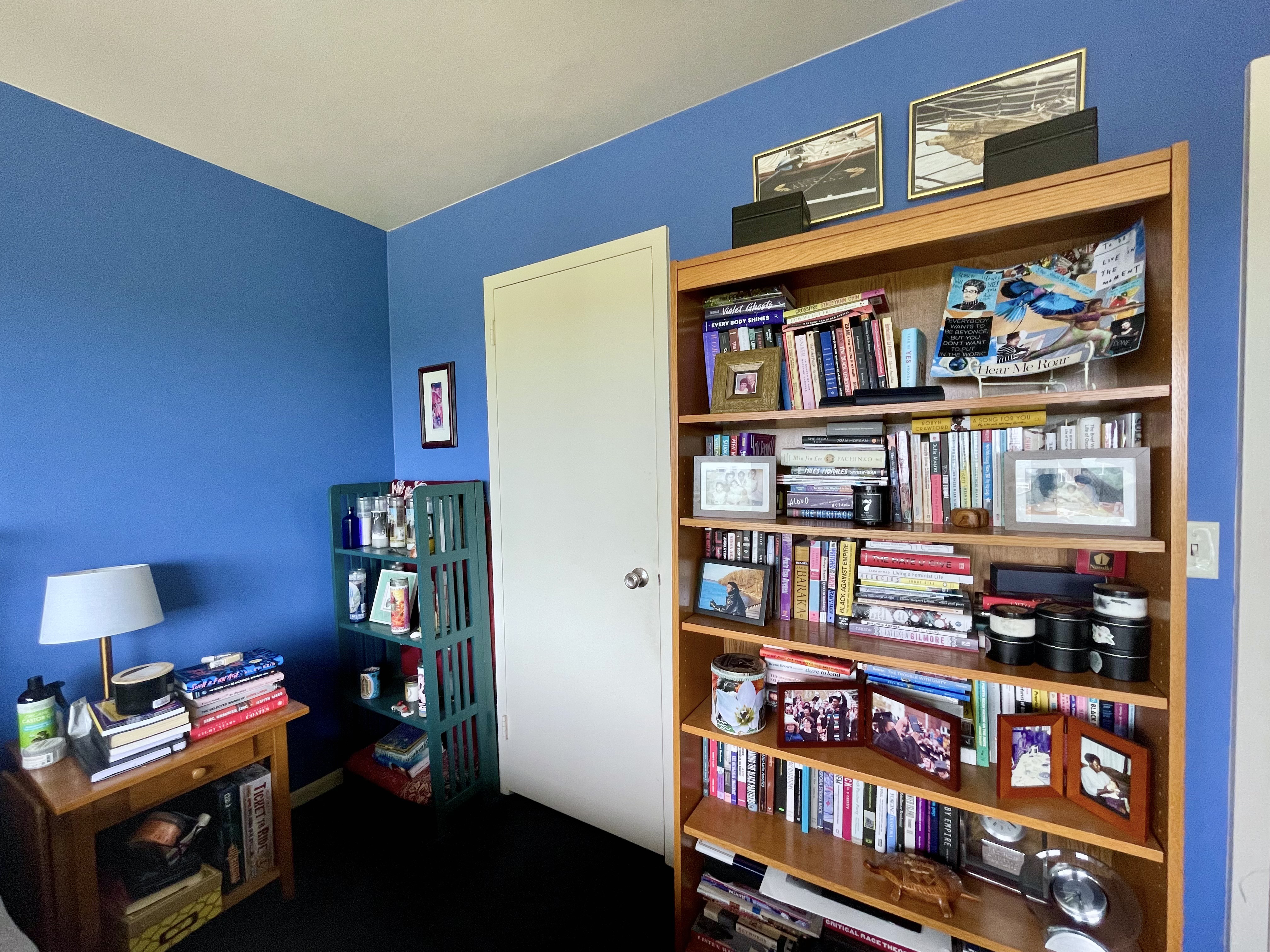 A photo of Carmen's bookshelf, which is piled high with books, alongside her altar full of candles and another pile of books on her nightstand.