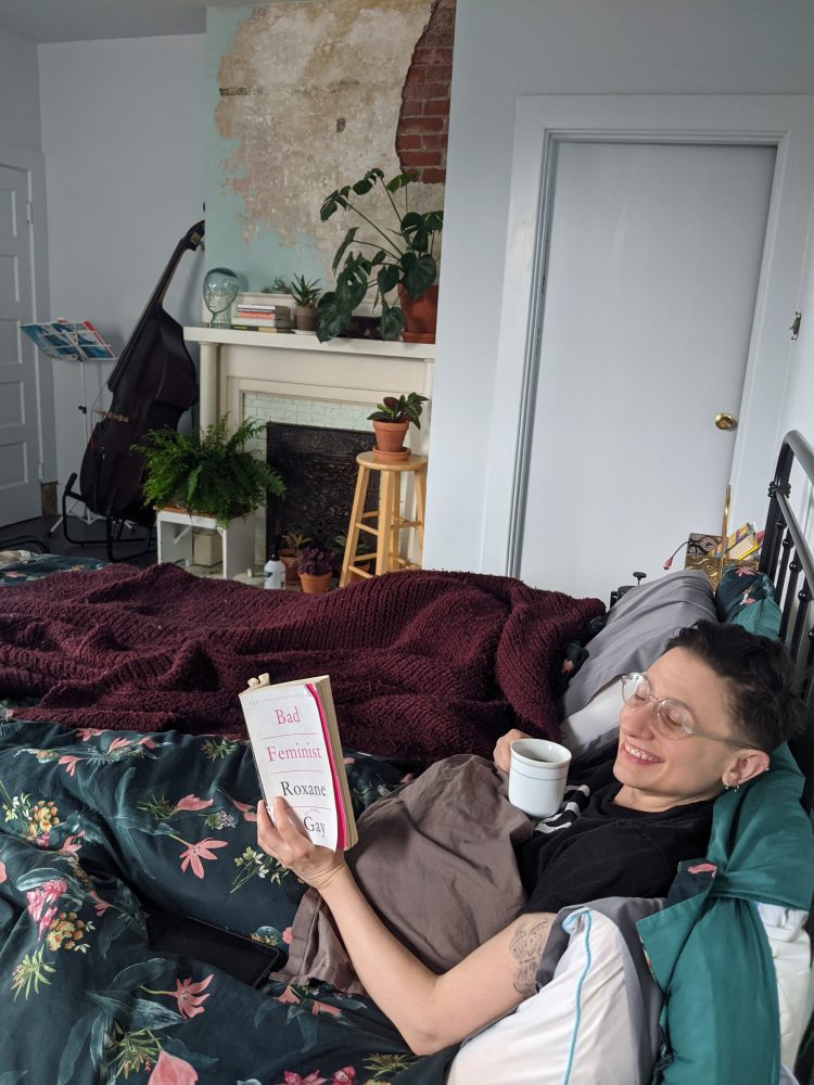 Sadie in our bed, reading Bad Feminist by Roxane Gay with a cup of coffee