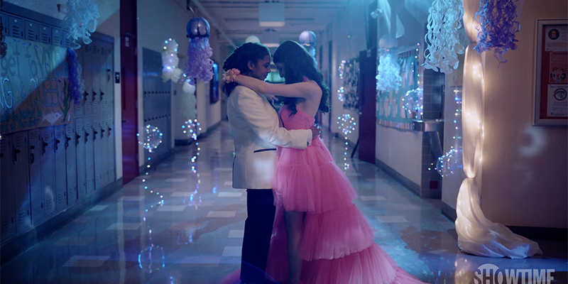 The L Word Generation Q Season 2 Trailer: Angie dances with her prom date. She wears a white jacket and black pants, her date is in a pink dress.