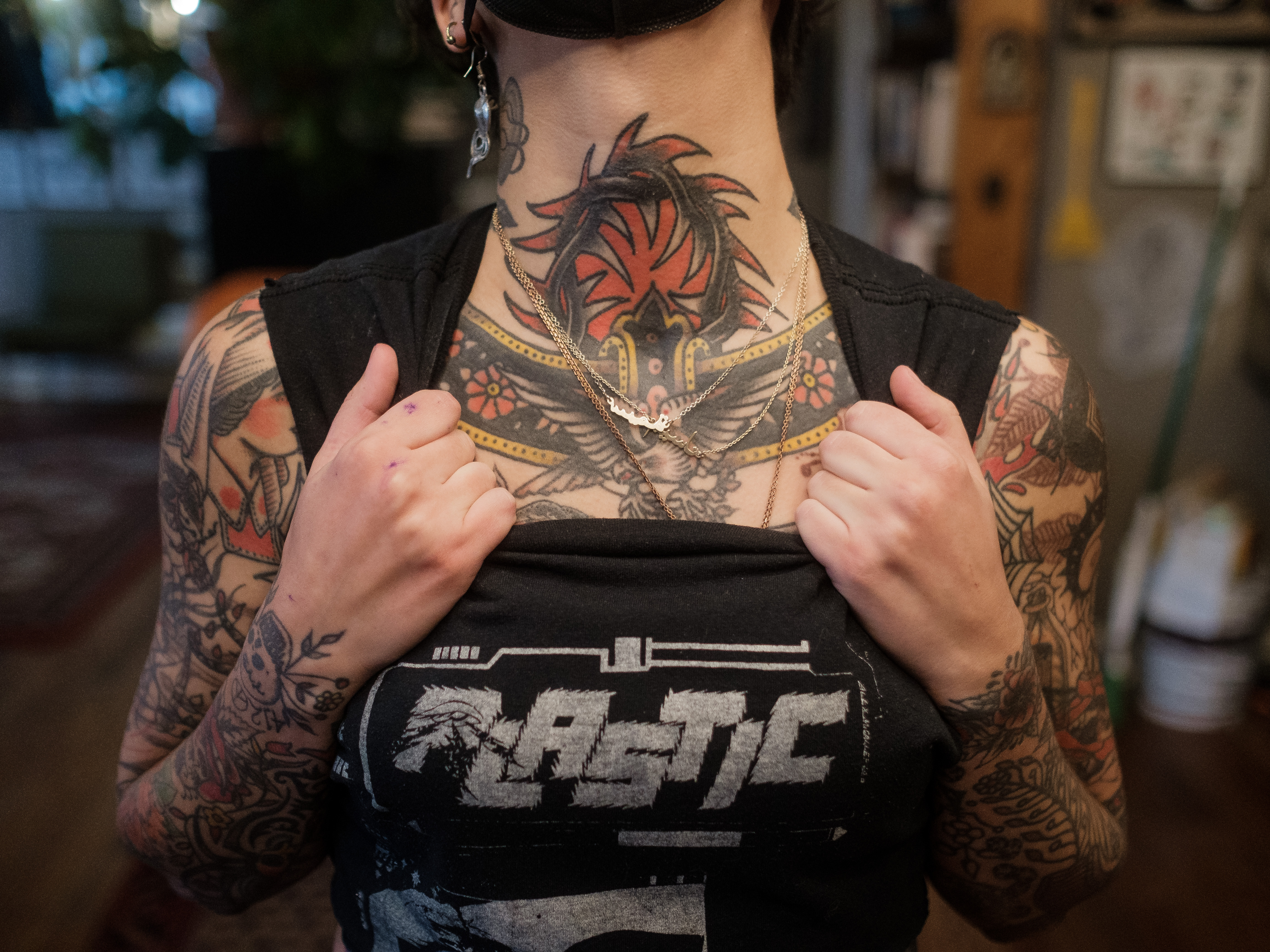 Image shows the heavily tattooed neck of Sema. They are holding their shirt down from the collar and their neck is lifted up.