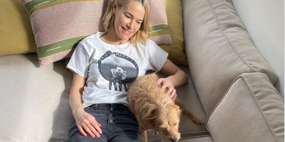 A cropped photo of Leisha Hailey gazing adoringly at a small dog while reclined on a sofa