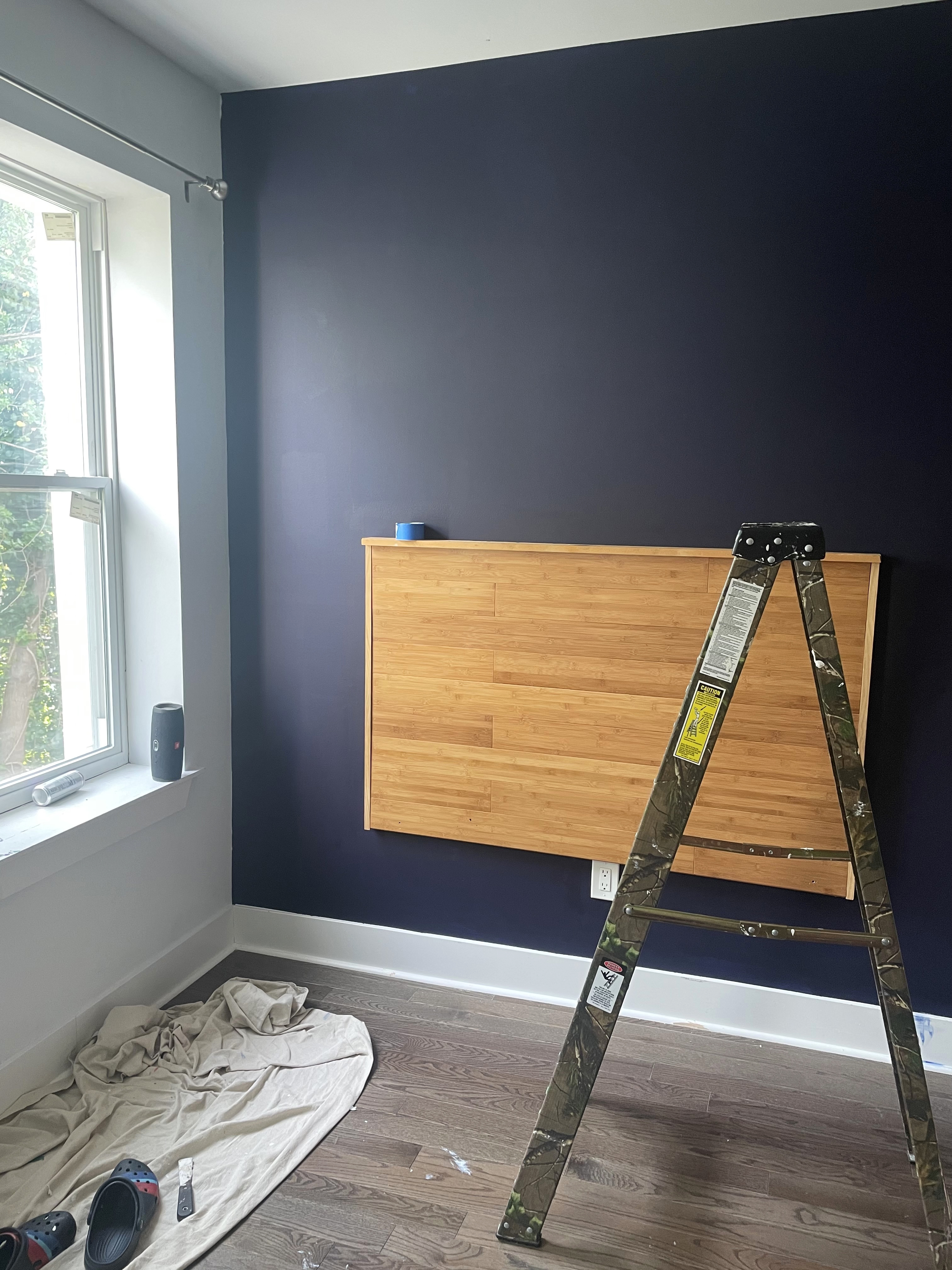 A dark purple wall with a wooden headboard mounted on the wall, a ladder and a pair of Crocs in the foreground