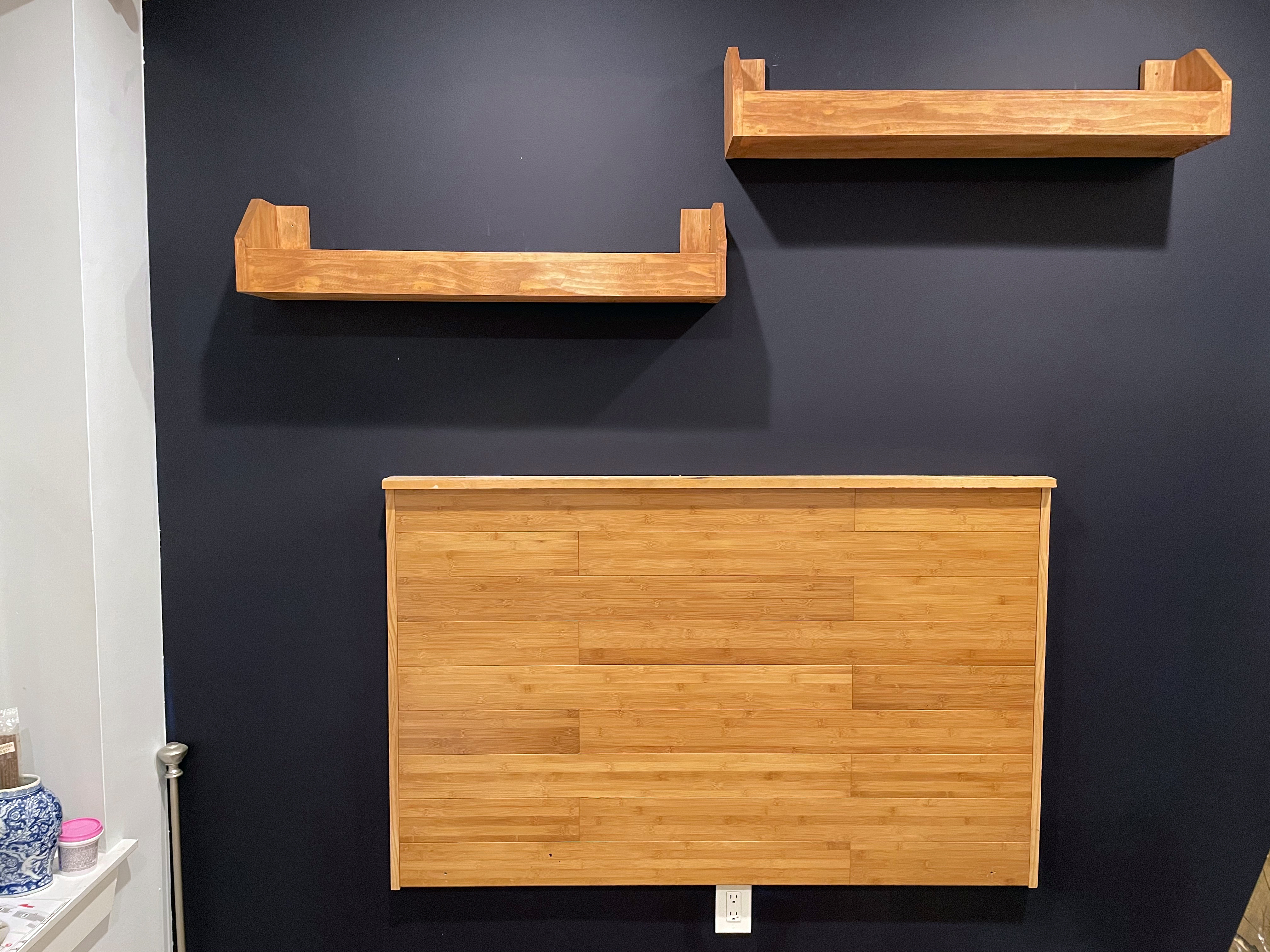 A wooden headboard and two bookshelves mounted on a dark purple wall