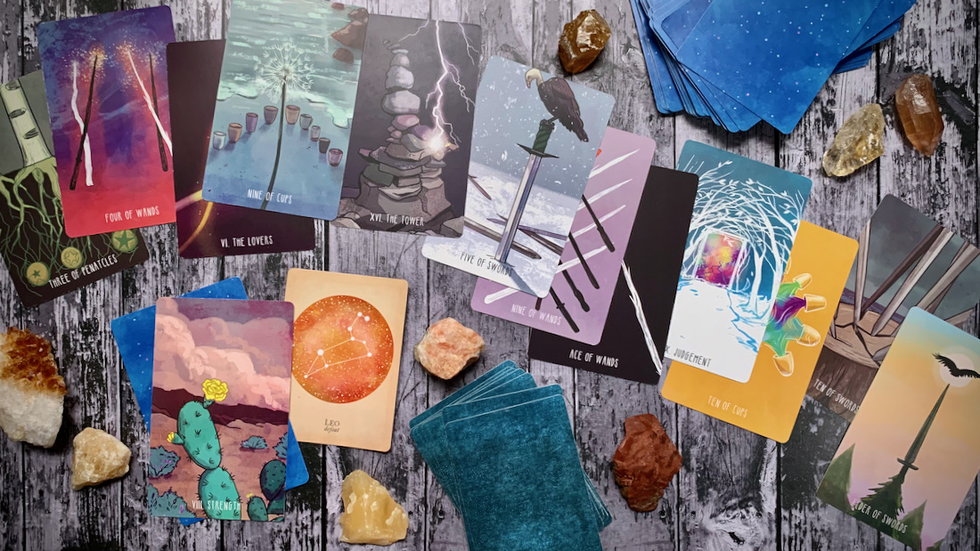 A scattered pile of beautiful brightly colored tarot cards and crystals across a wooden surface.