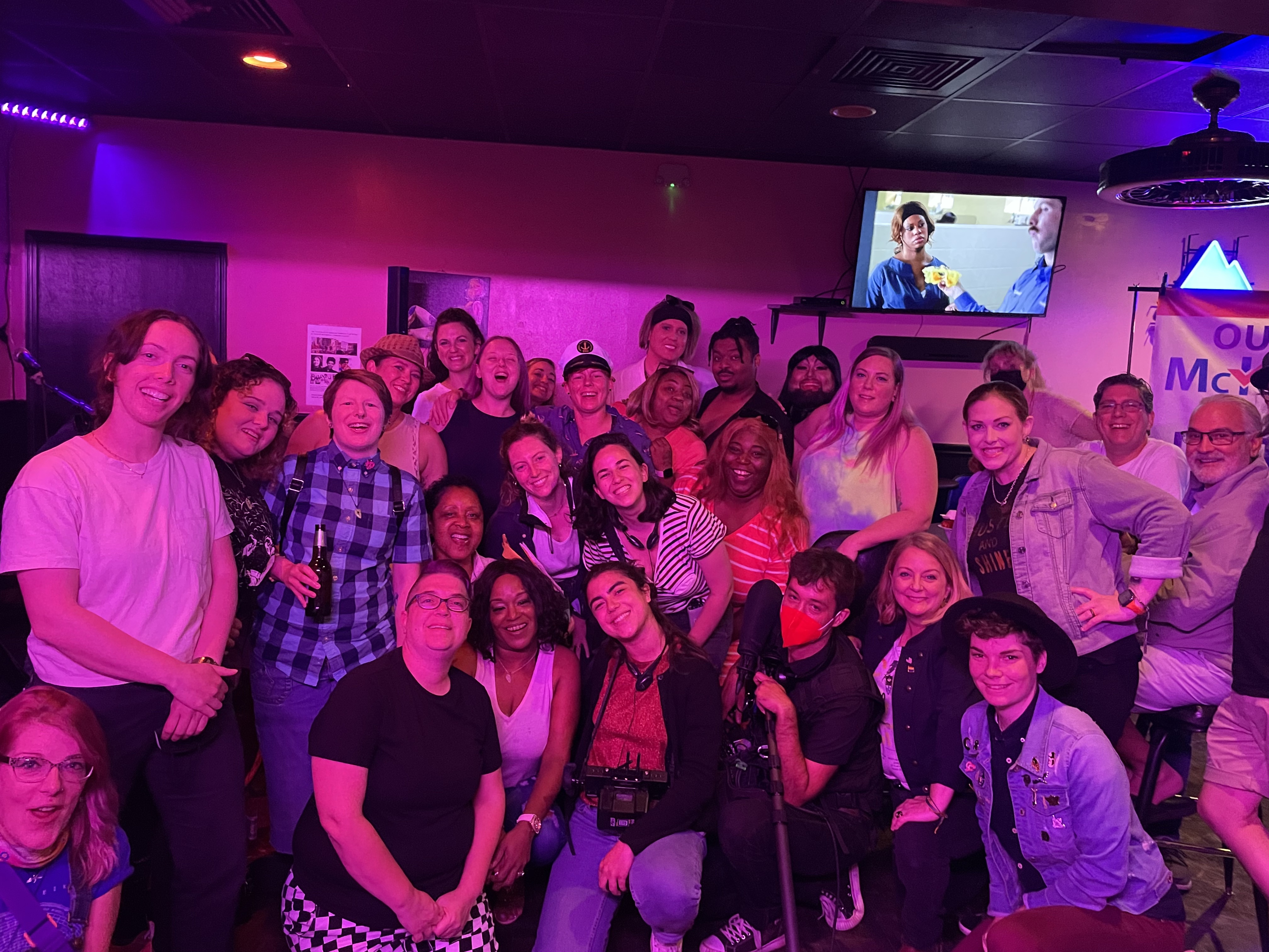 A huge group gathers at Herz, a lesbian owned bar in Mobile, Alabama. Everyone is smiling and looks happy.