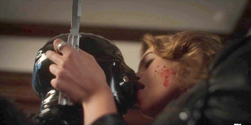 Ruby and Scarlett kiss post-kill. Scarlett wears the rubber suit and Ruby holds a bloody knife.