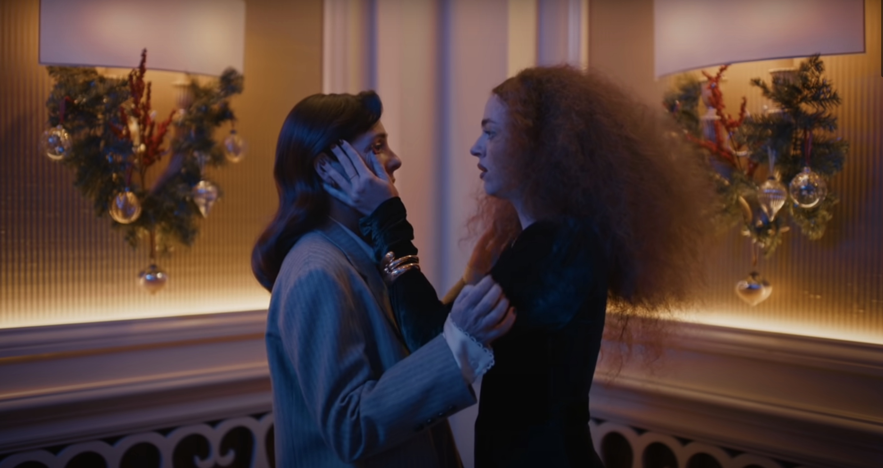 Two fancy women holding each other's faces like they're about to kiss