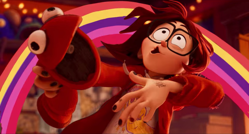 An animated teen girl with glasses and black nail polish leans back in front of a rainbow while wearing a red puppet.