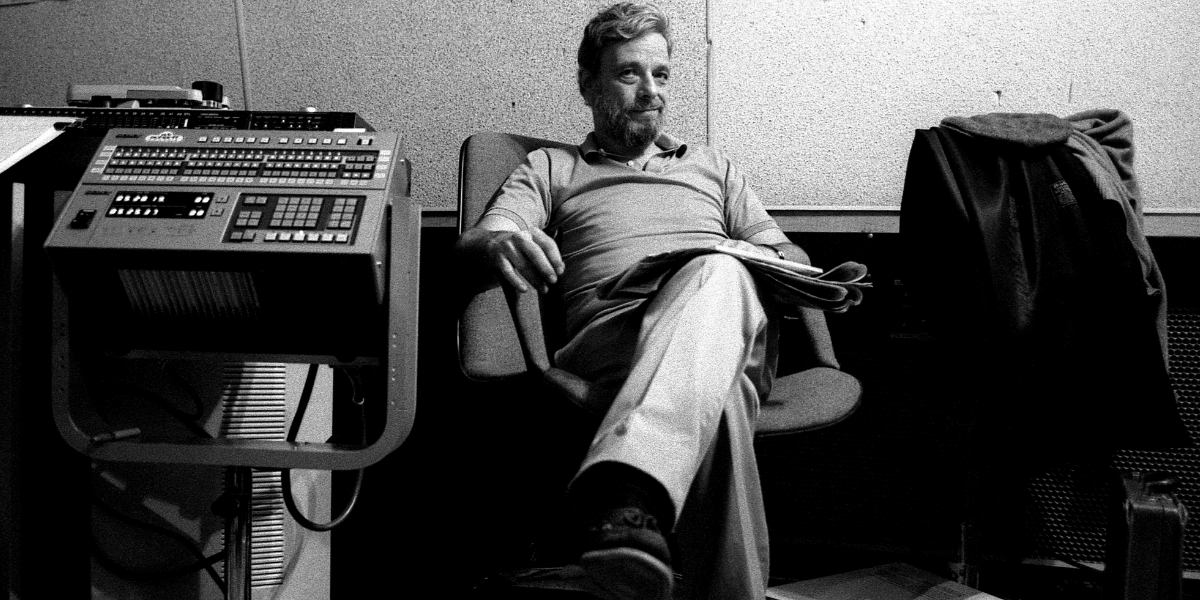 A black and white photo of Stephen Sondheim sitting in a chair smirking