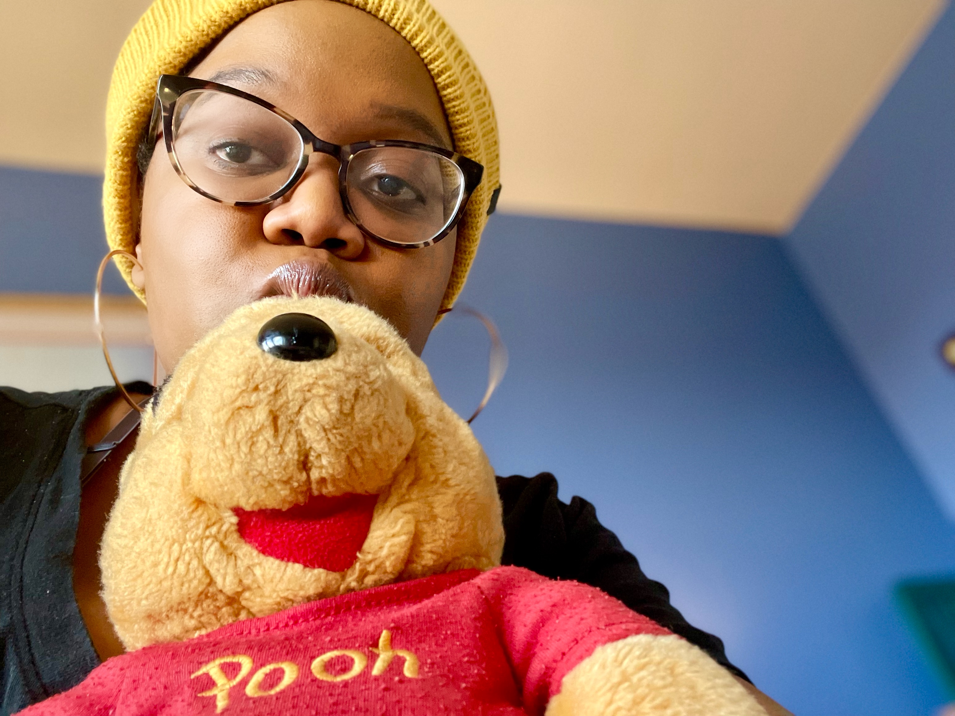 Winnie-the-Pooh and Carmen are matching in yellow and Carmen holds Winnie while making a face at the camera.