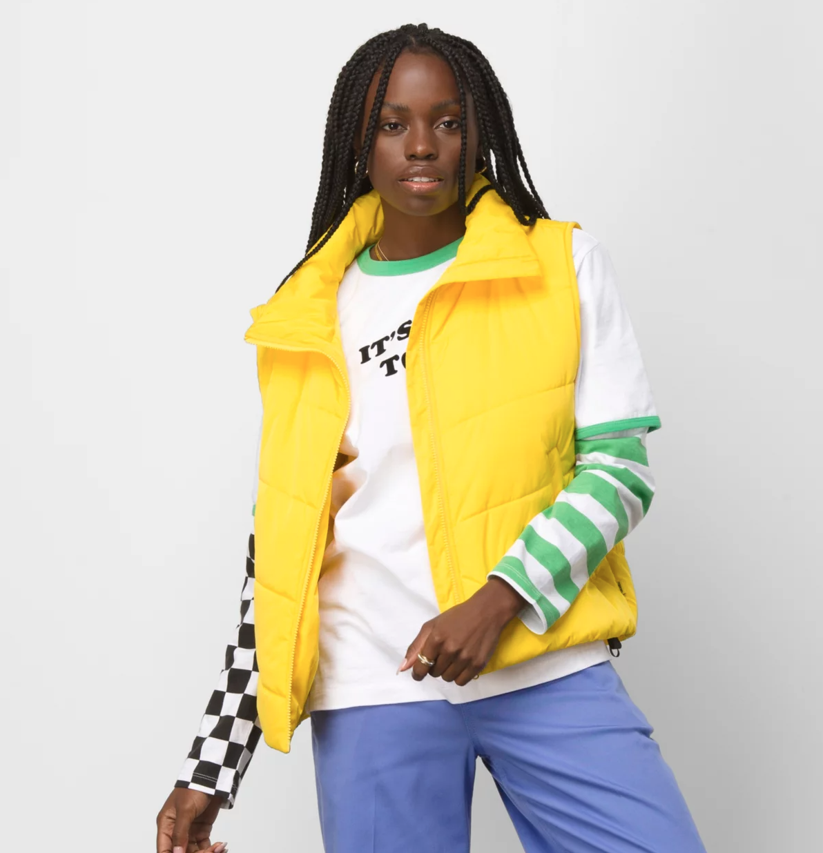A person wearing a yellow puffer vest over a long sleeved shirt and blue pants